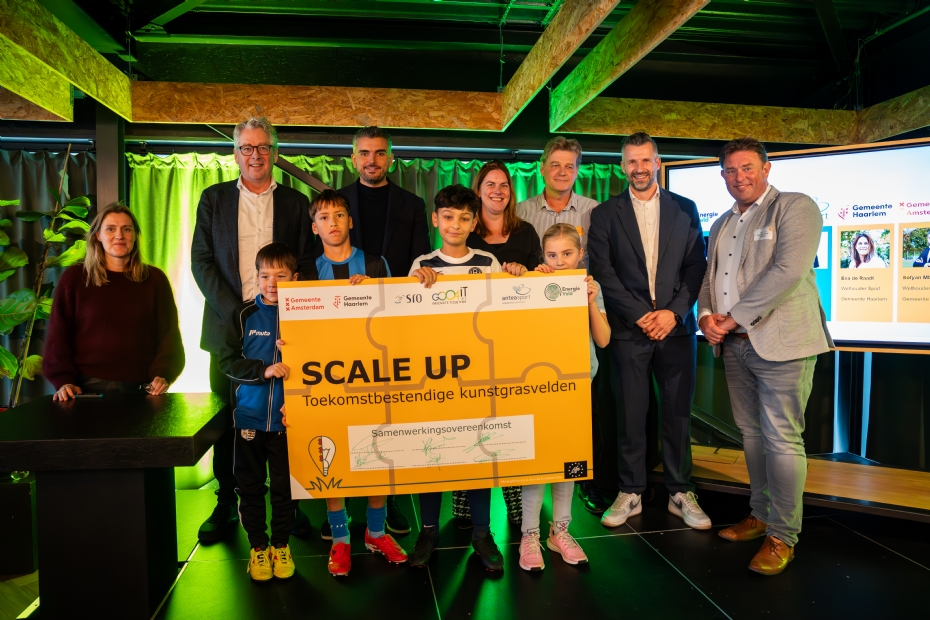 Jonge sporters tonen het ondertekende startdocument met op de achtergrond de wethouders en vertegenwoordigers van de consortia.